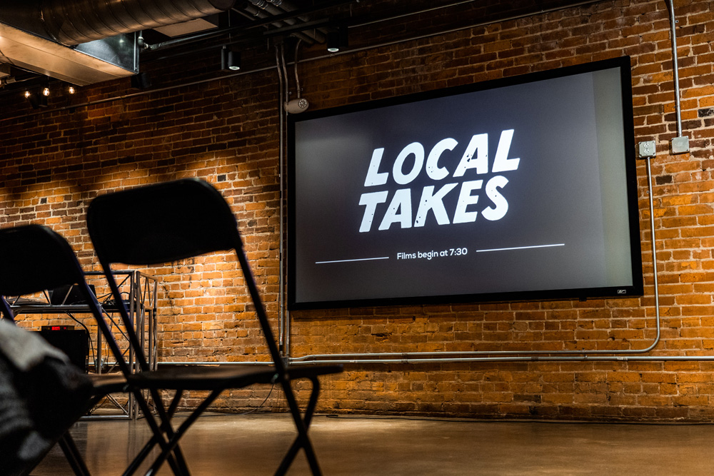 An empty chair in front of film projecting “Local Takes” at the film premiere